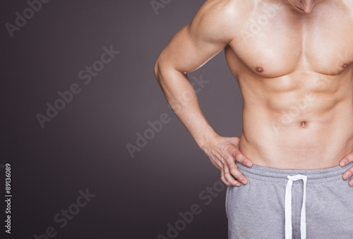 Fitness man showing six pack abs on grey background