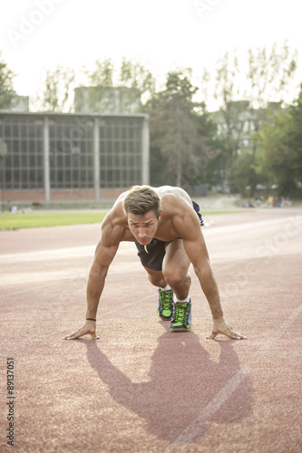 Sprinter at start position, kneeling, muscular body.