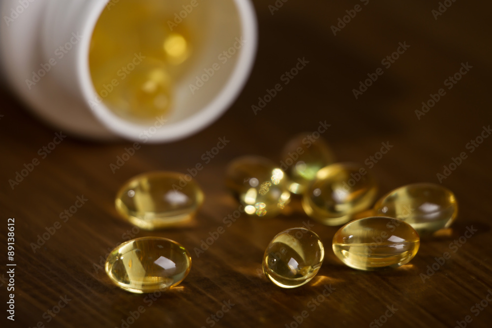 Capsules of fish oil spilled out open container on wooden table Capsules of fish oil spilled out open container on wooden table