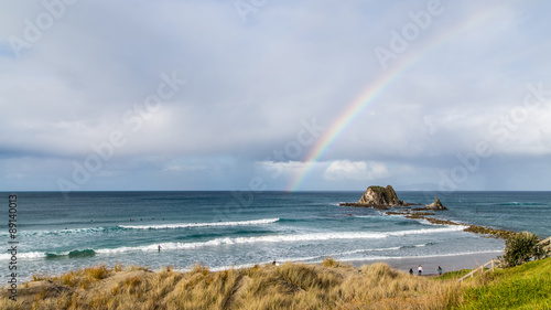 Rainbow at rocky beach with surfers