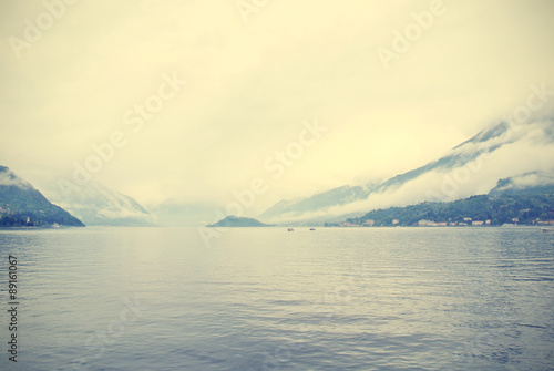Landscape on Lake Como, Italy, on a cloudy, foggy morning, with lake shores shrouded in mist. Image filtered in faded, washed out, retro, Instagram style.