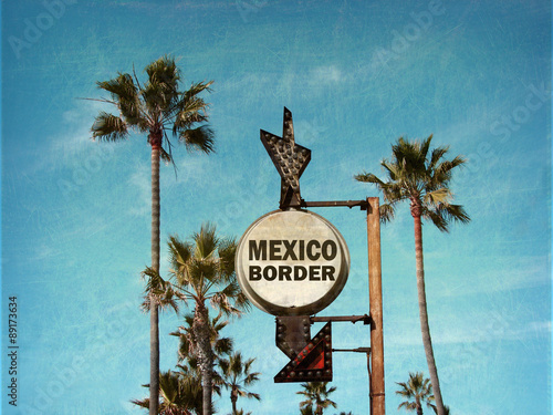 aged and worn vintage photo of mexico border sign with palm trees