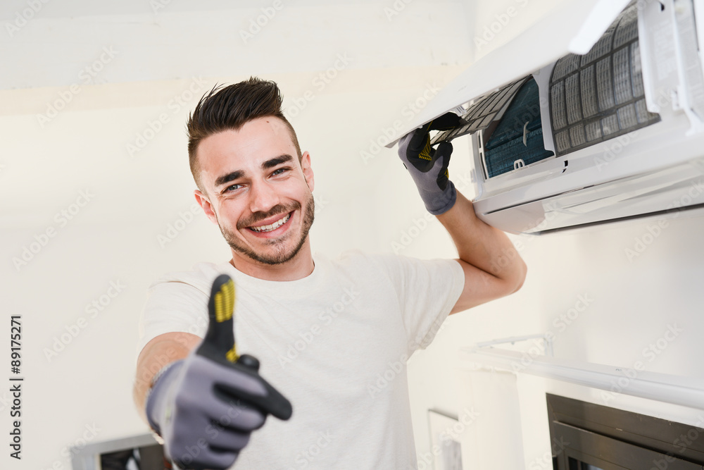 handsome young man electrician installing air conditioning in a client house - obrazy, fototapety, plakaty 