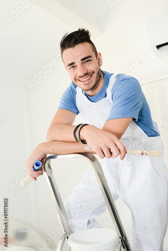 handsome young man professional painter applying white paint in wall with roller