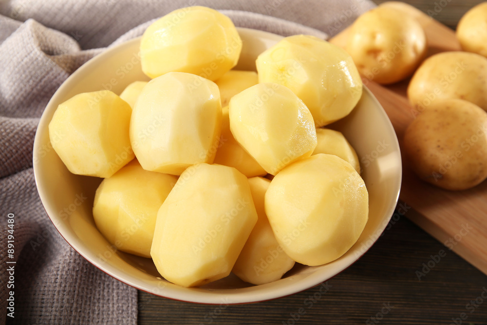 Peeled new potatoes in bowl on wooden table with napkin, closeup