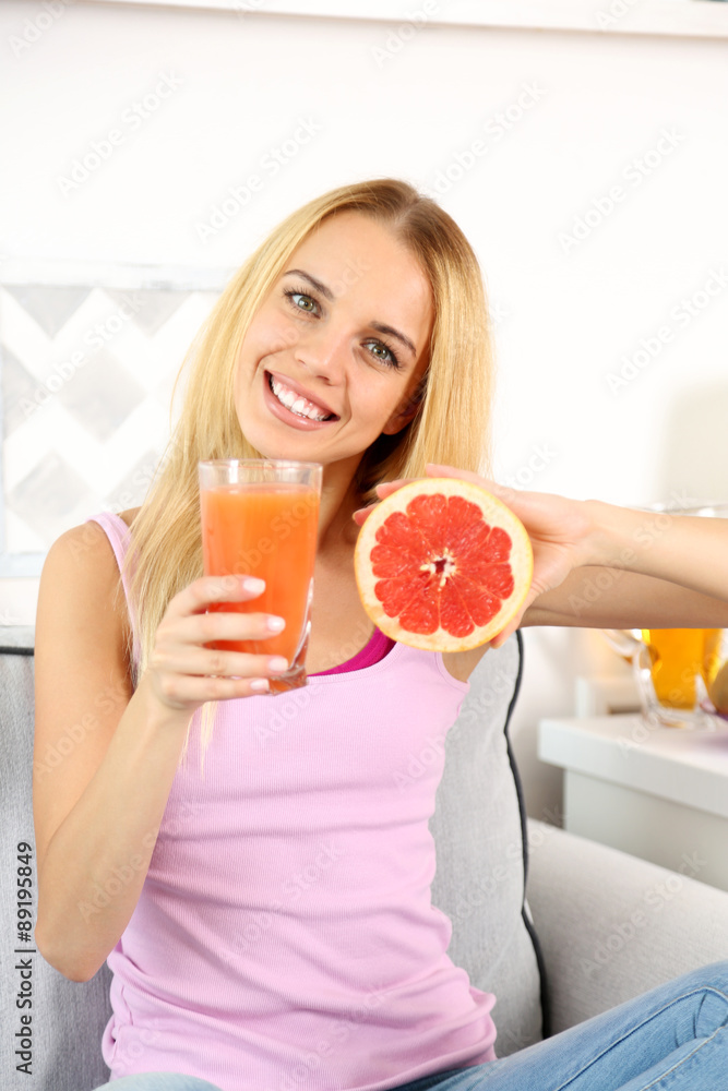 Young beautiful woman sitting on sofa with glass of fresh grapefruit juice Young beautiful woman sitting on sofa with glass of fresh grapefruit juice