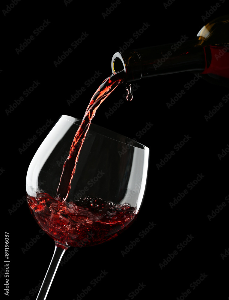 Fototapeta premium Red wine pouring into wine glass on black background