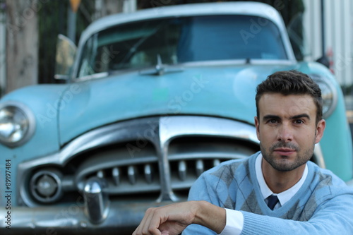 A young handsome man and a classic car in the background 