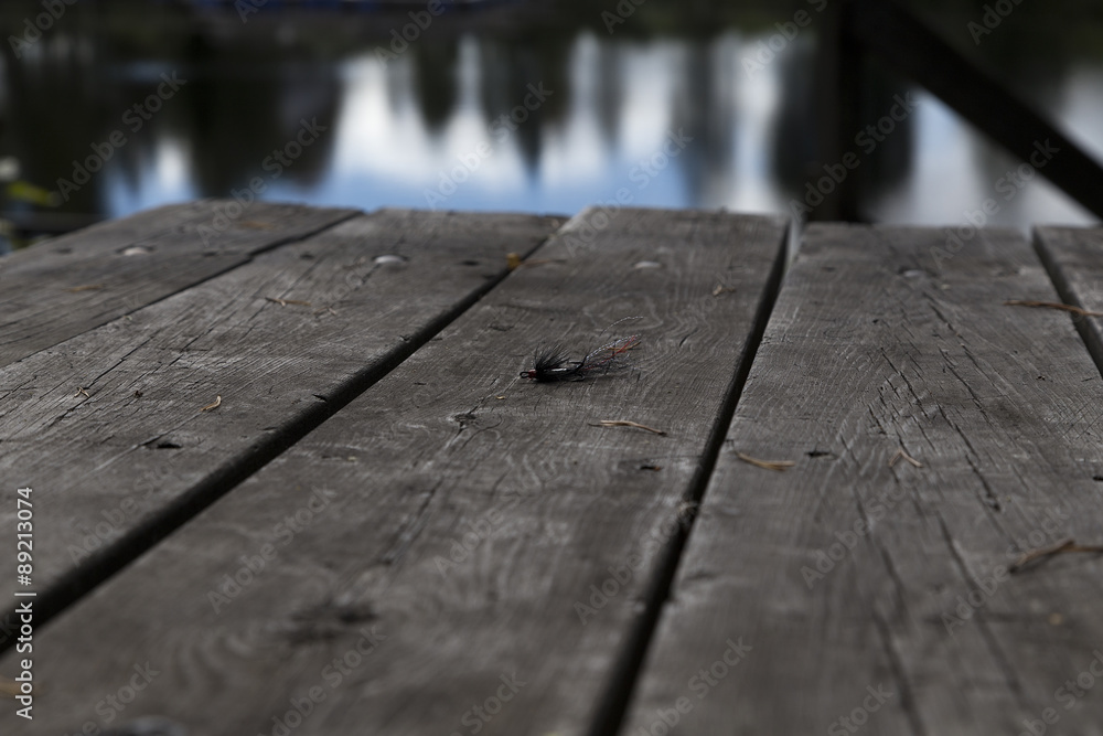 Fototapeta premium A lure with feathers on a table of wood and reflections from the water