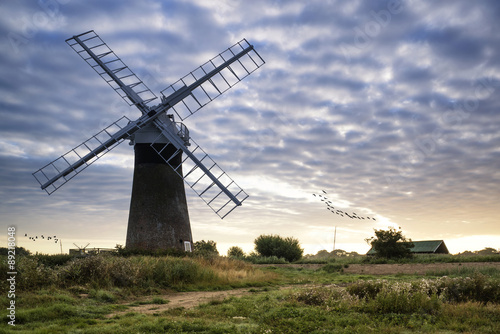 Old pump windmill in English countryside landscape early morning