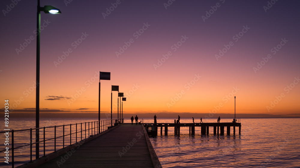 Silhouettes of people walking on a pier at sunset