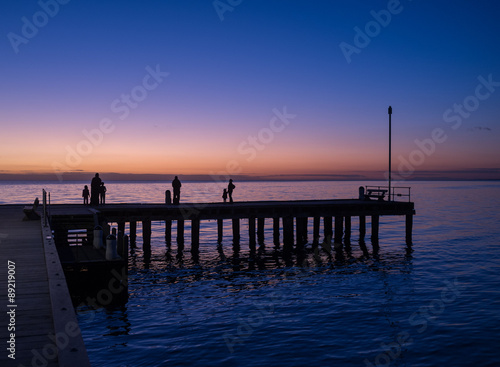 Silhouettes of people standing on a pier at sunset