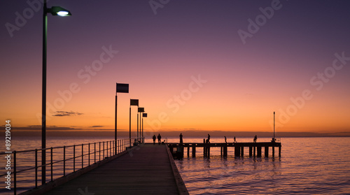 Fototapeta Naklejka Na Ścianę i Meble -  Silhouettes of people walking on a pier at sunset
