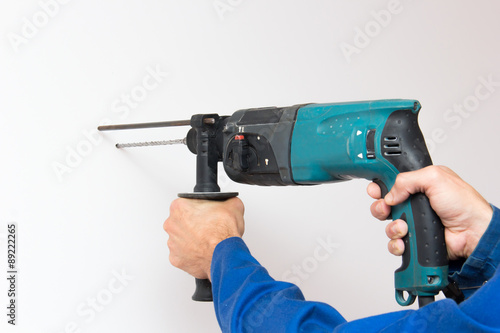 Construction worker is boring the wall by electric perforator