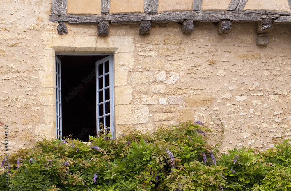 Window Decorated with Wisteria. An old historical building in a market village in France has a window decorated with wisteria.