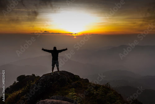 Hiker open arms on peak of mountain at sunset.