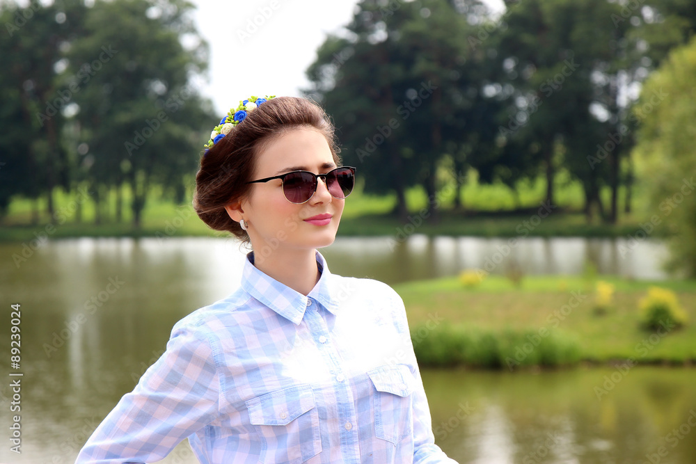 Portrait of young beautiful girl in sunglasses and in blue shirt. Young free woman. Student. Beautiful, cute woman near lake Portrait of young beautiful girl in sunglasses and in blue shirt. Young free woman. Student. Beautiful, cute woman near lake