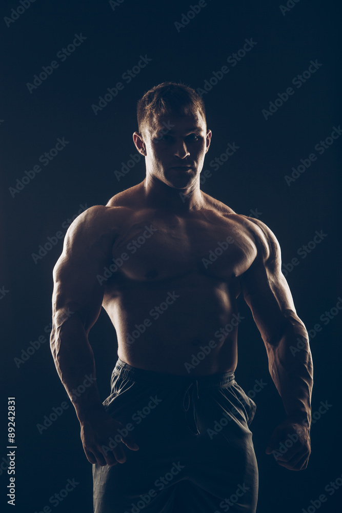 Fototapeta premium Handsome muscular bodybuilder posing over black background.