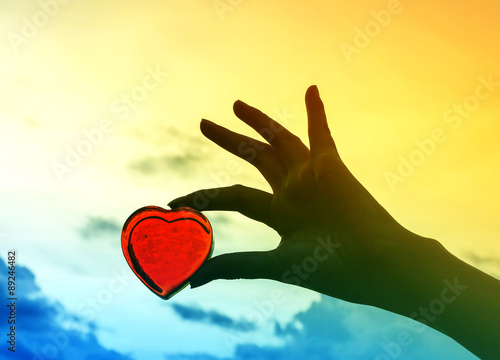 Art tone of red heart glass in silhouette hand on evening sky background