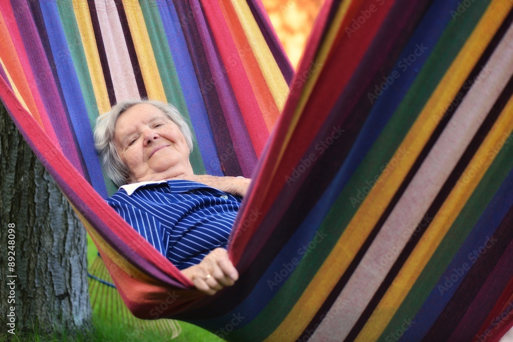 Senior happy woman resting on a hammock in garden.