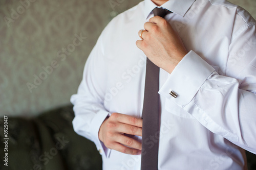 Man in a white shirt with cuff links, straightens his tie