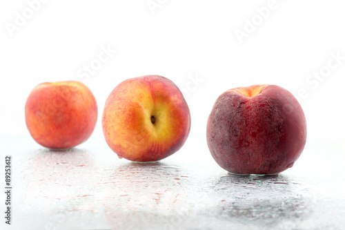 three ripe peaches in the water droplets on white background