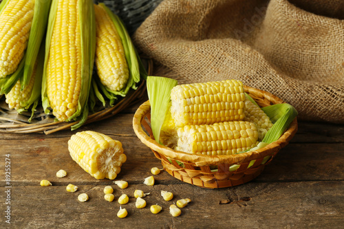Fresh corn on cobs in wicker bowl on wooden table with sackcloth, closeup