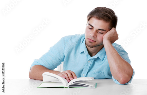 Young man reading book at table on white background