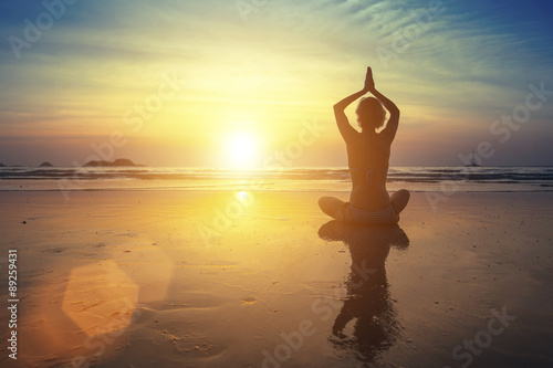Young woman practicing yoga on the beach at amazing sunset (with reflection)