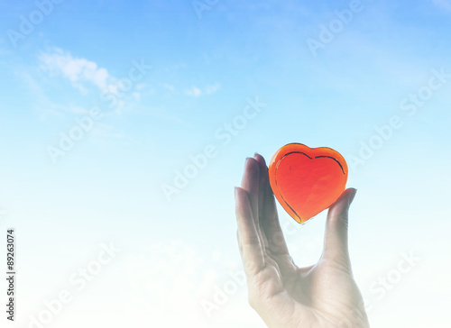 Art tone of red heart glass in hand on blue sky background