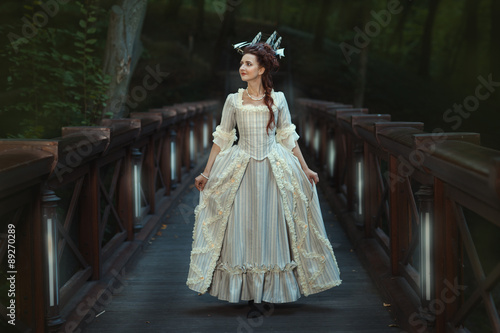 The girl in an old ball dress walking on bridge.