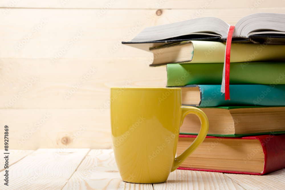 Obraz premium Stack of colorful books, open book and cup on wooden table. Back to school. Copy space