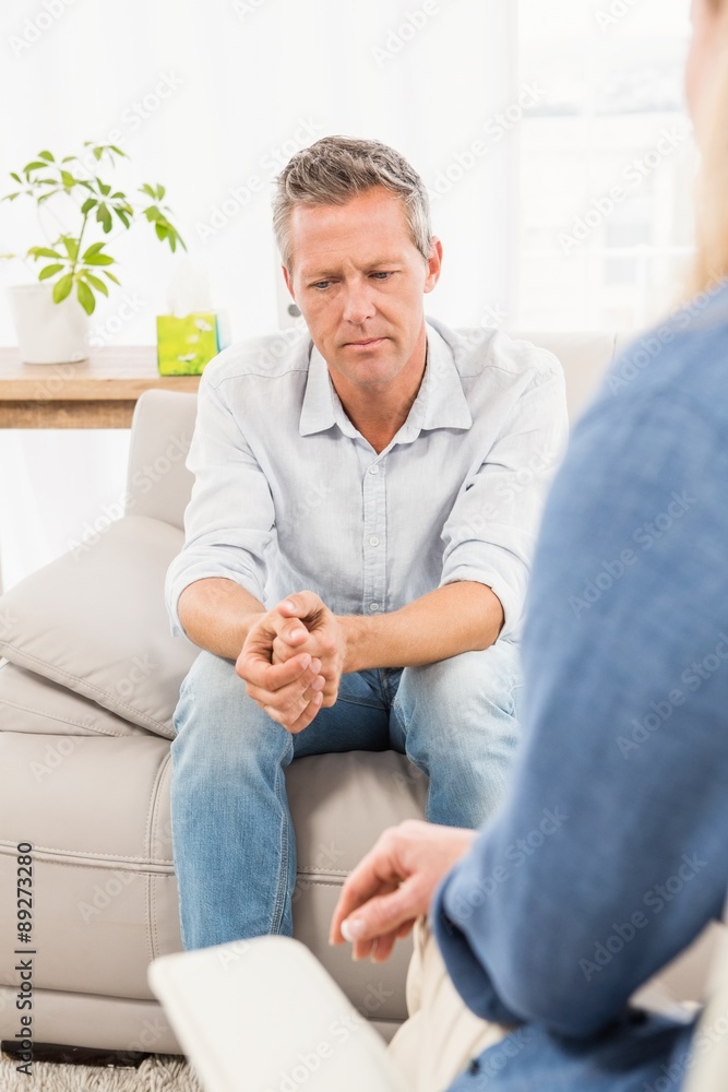 Worried man sitting on couch and talking to therapist 