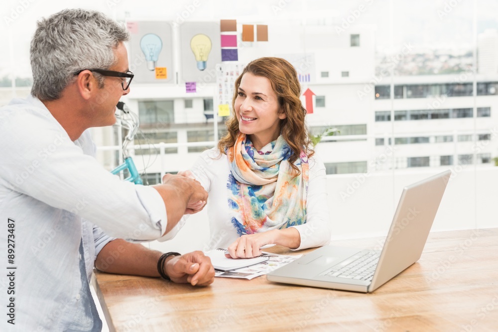 Smiling casual designers sitting and handshaking Smiling casual designers sitting and handshaking