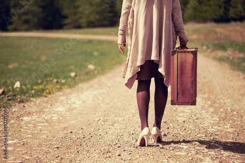 Woman walking on country road with old suitcase, intentionally toned.