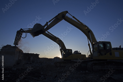 The bucket excavator and the excavator with a hammer are working on clearing the construction site