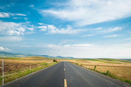 Fotografie An open road on a field, under the blue sky