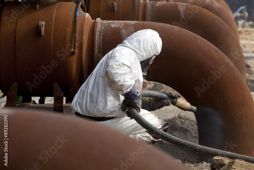 Worker in protective equipment cleans the metal construction before painting them