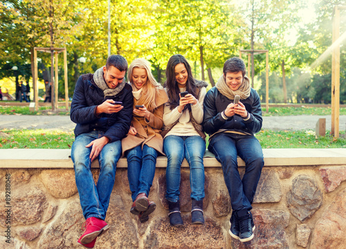 smiling friends with smartphones in city park © Syda Productions
