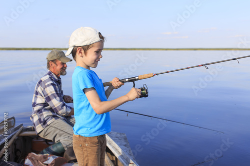 Fishing boat.Grandfather and grandson fishing together on a spinning sitting in a boat on a river