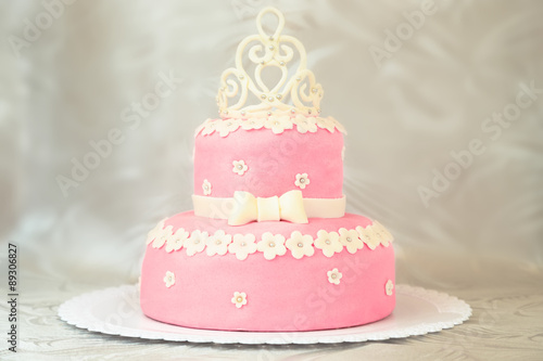 Pink cake with a crown on a white plate over a white tablecloth