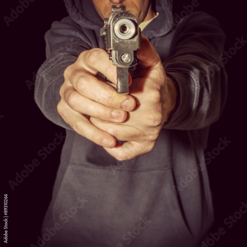 hooded man pointing hand held gun towards camera