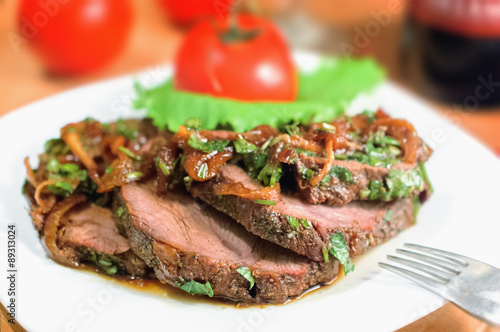 Beef sliced with a sauce of grilled onions and parsley on a white plate