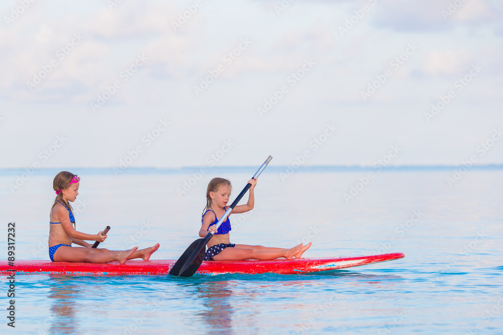 Little cute girls swimming on surfboard during summer vacation