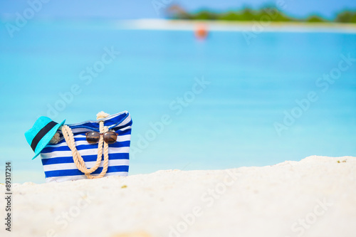 Blue bag, straw hat, sunglasses and sunscreen bottle on white