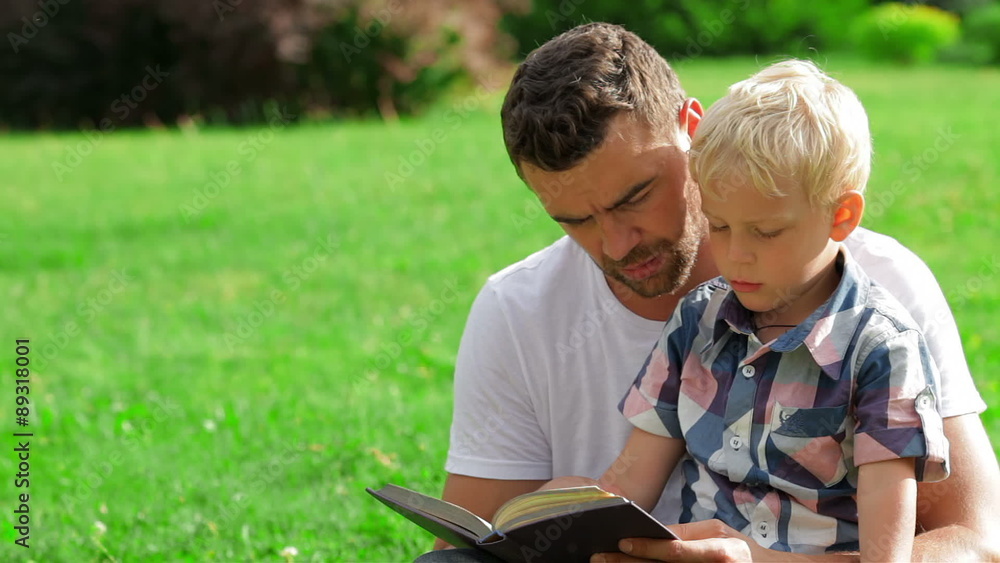 Father and son reading book in park Father and son reading book in park