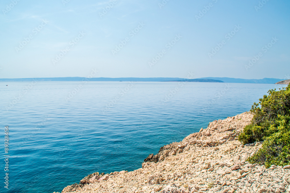 Rocky coastline with crystal clear blue Adriatic sea with island