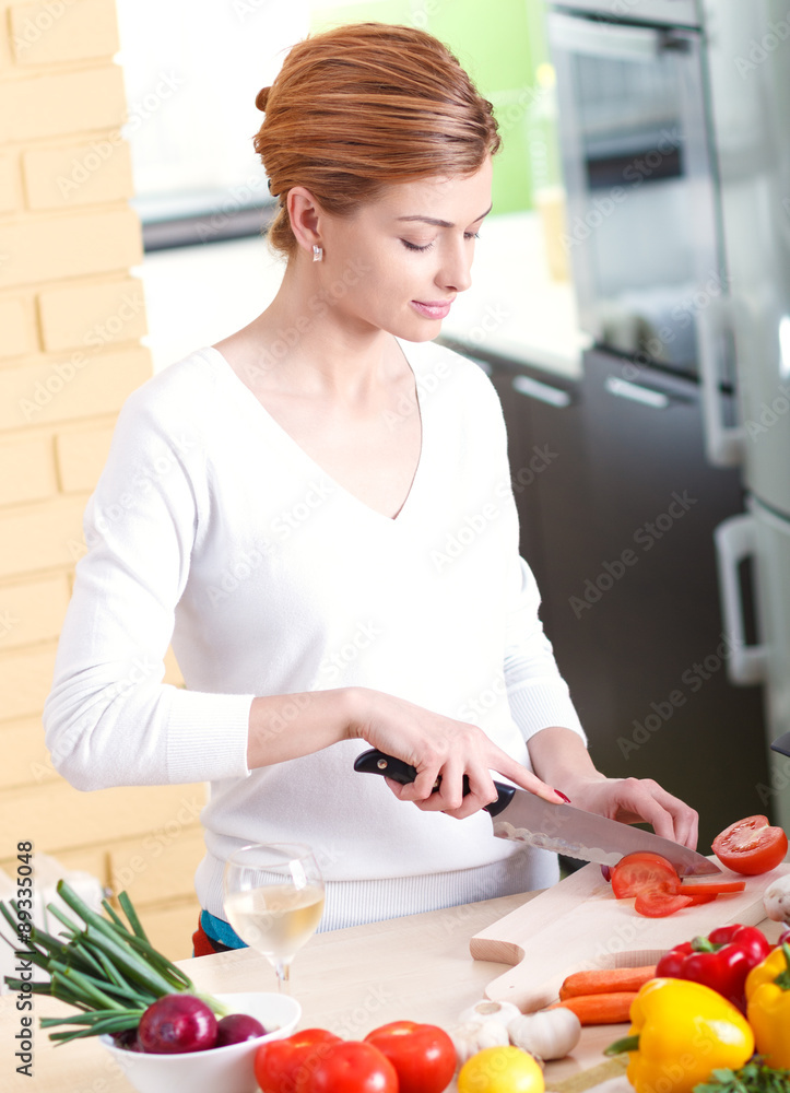 Smiling young woman cutting vegetables in kitchen.