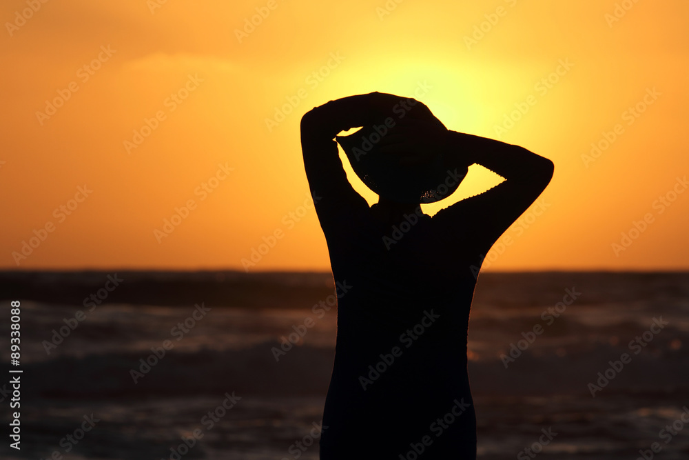 Fototapeta premium female form with the hat against the sea at sunset