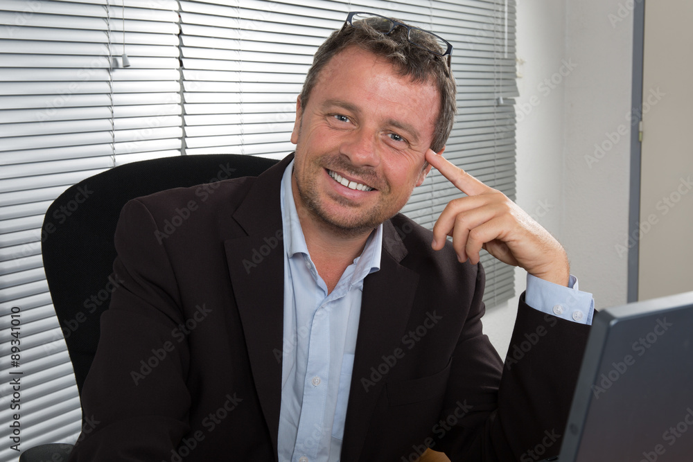 Creative professional at work. Handsome young man in shirt working on laptop in front of his desk and smiling while sitting at office Creative professional at work. Handsome young man in shirt working on laptop in front of his desk and smiling while sitting at office